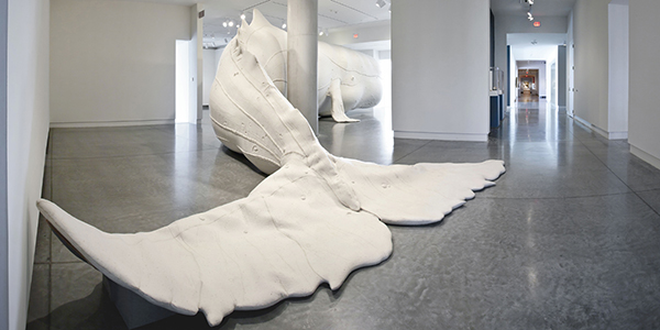VMFA Exhibit 2011. Tristin Lowe: Mocha Dick Jul 23 – Nov 27, 2011 21st Century Gallery photo: Travis Fullerton ©Virginia Museum of Fine Arts Tristin Lowe’s colossal sculpture Mocha Dick is a fifty-two-feet-long recreation of the real-life albino sperm whale that terrorized early 19th-century whaling vessels near Mocha Island in the South Pacific. Mocha Dick, described in appearance as “white as wool,” engaged in battle with numerous whaling expeditions and inspired Herman Melville’s epic Moby-Dick (1851). Lowe worked with the Fabric Workshop and Museum in Philadelphia to make the sculpture: a large-scale vinyl inflatable understructure sheathed in white industrial felt. Tristin Lowe’s massive sculpture takes its name, anatomy, color, and inspiration from a legendary albino sperm whale that inhabited the South Pacific waters near Mocha Island in the early 19th century. Vividly chronicled by a New England seafarer and published in the monthly Knickerbocker magazine (1839), the creature was said to have attacked as many as twenty whaling vessels. The graphic account describes the elusive behemoth, known as Mocha Dick, as a ghostly presence: “As white as wool . . . as white as a snow drift . . . white as the surf around him.” This notorious creature was especially striking because sperm whales are commonly dark gray, brown, or black. The great 19th-century work of art that also drew its inspiration from this infamous white whale is Herman Melville’s epic Moby-Dick, published in 1851. Lowe’s reckoning with the mythic mammal can be traced to his fascination with Melville’s novel and his research into maritime history. He built his fifty-two-foot sculpture true to the scale of a sperm whale. The work has a coat of thick wool felt covering an inflated vinyl armature. Clusters of handcrafted barnacles are appliquéd to the whale’s body and scar-like stitches zigzag across its surface. These naturalistic embellishments attest to the creature